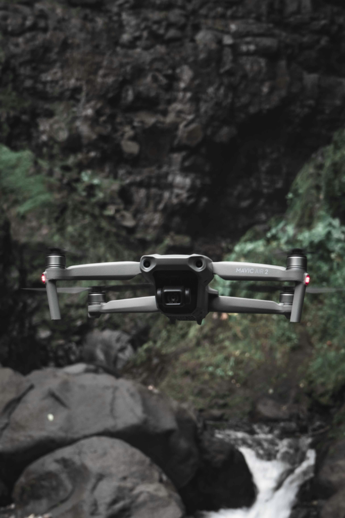 A close-up shot of a drone flying near a rocky waterfall in a lush environment.